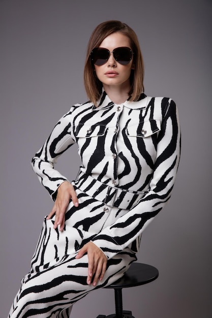 Elegante donna in bella stampa zebrata giacca gonna stivaletti neri occhiali da sole sfondo grigio