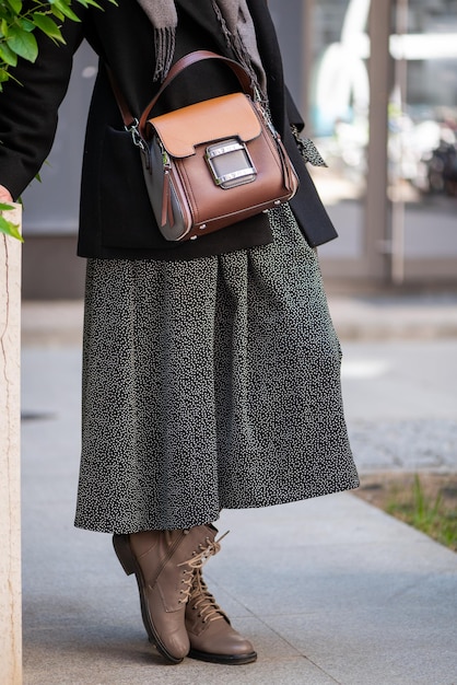 Elegant woman in trendy dress and coat and leather shoes with stylish bag hanging across shoulder