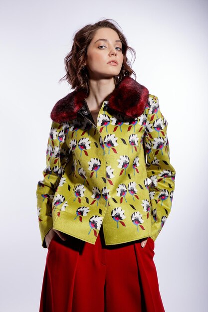 Elegant woman in yellow jacket with pattern flowers red trousers pants posing on white background