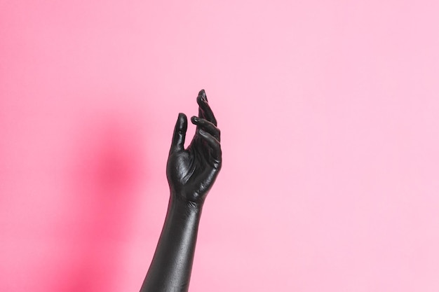 Elegant womans hand with black paint on her skin on pink background High Fashion art concept