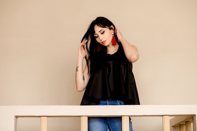 An elegant young Asian brunette in jeans and a black blouse is dancing on the balcony . Interior in mustard colors .