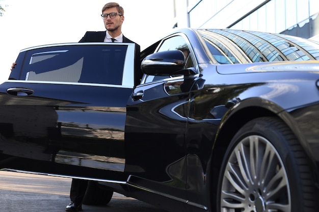 Foto elegante giovane uomo d'affari che entra nella sua auto mentre si trova all'aperto.