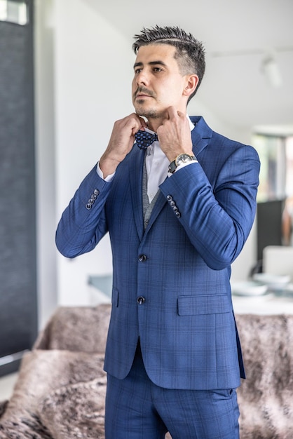 Elegant young groom fastens his tie on his wedding day during preparations