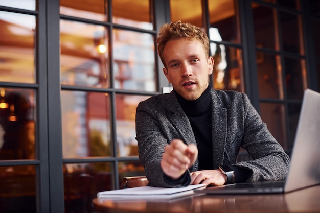 Elegant young guy in formal wear sits in cafe with his laptop.