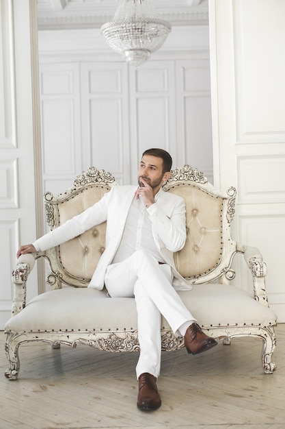 Elegant young handsome man with a beard in a white classic suit