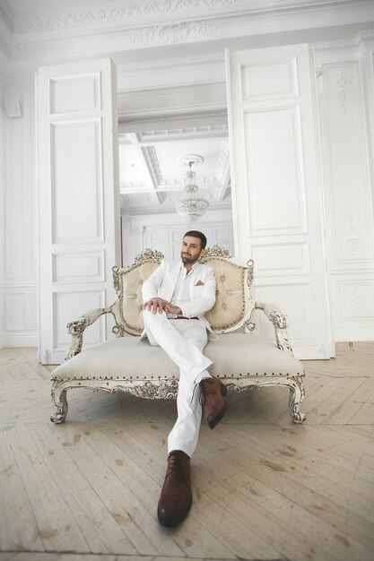 Elegant young handsome man with a beard in a white classic suit