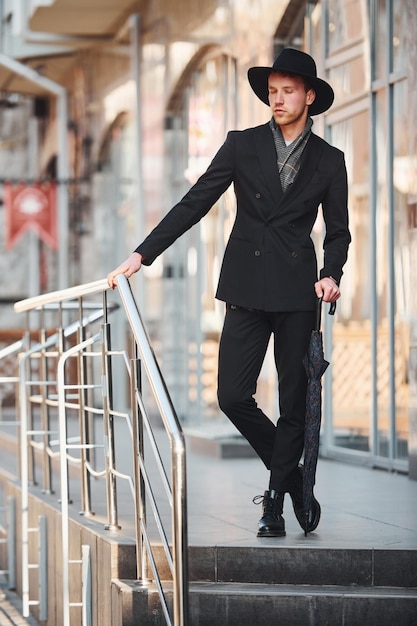 Elegante giovane con cappello nero e con ombrello all'aperto in città