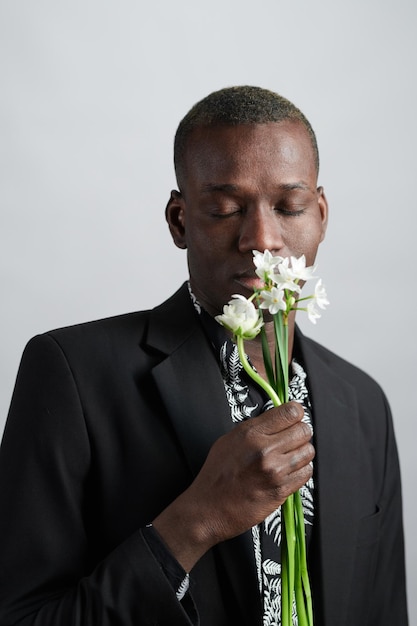 Elegant young man in jacket and shirt smelling flowers