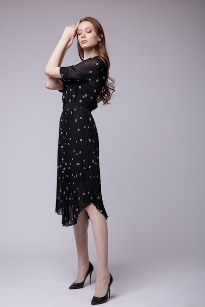 Elegant young woman in black dress with small white flowers on white background Studio Shot