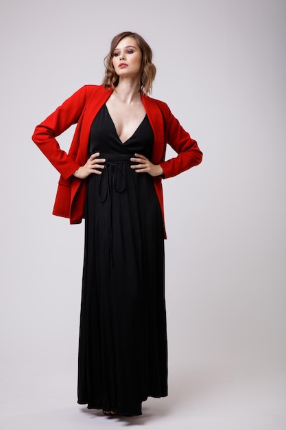 Elegant young woman in black evening party dress with deep neckline red jacket on white background