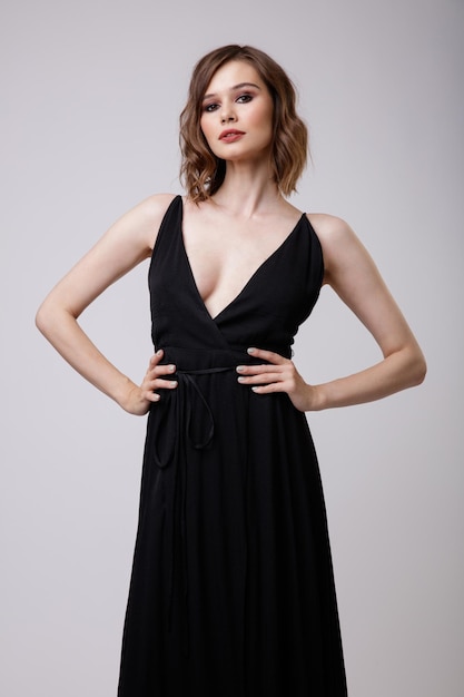 Elegant young woman in black evening party dress with a deep neckline on white background