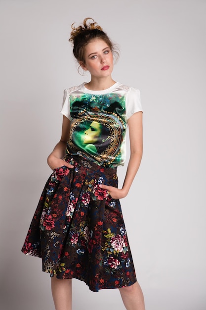 elegant young woman in black floral pattern long skirt, t-shirt posing on white background