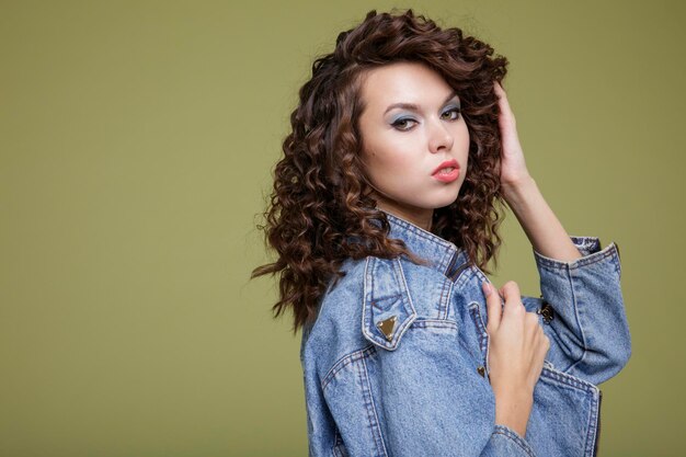 Elegant young woman in denim jeans jacket, blue trousers, white\
boots, posing over green background