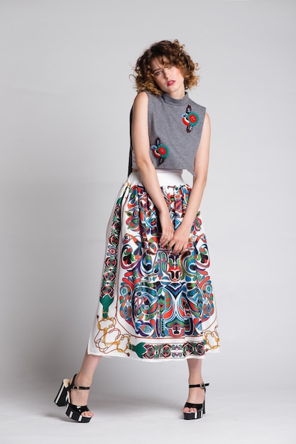 elegant young woman in gray top, pattern long skirt posing on white background