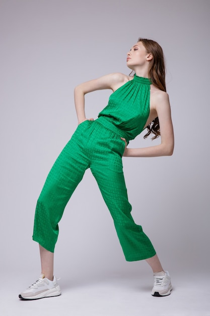 Elegant young woman in green jumpsuit sneakers on white background Studio Shot Full length