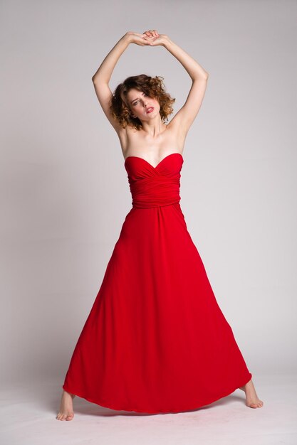 elegant young woman in long red dress posing on white background