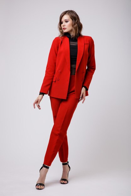 Elegant young woman in a pretty red suit jacket pants trousers black blouse on white background