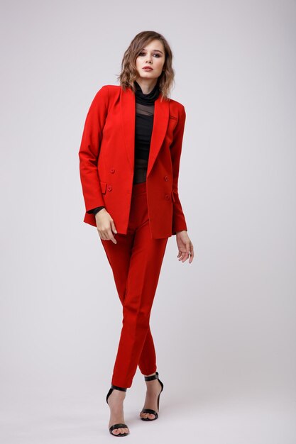 Elegant young woman in a pretty red suit jacket pants trousers black blouse on white background