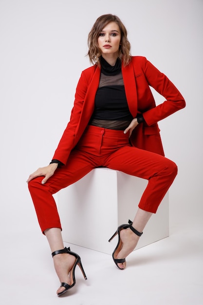 Элегантная молодая женщина в красивом красном пиджаке, брюках, брюках, черной блузке на белом фоне