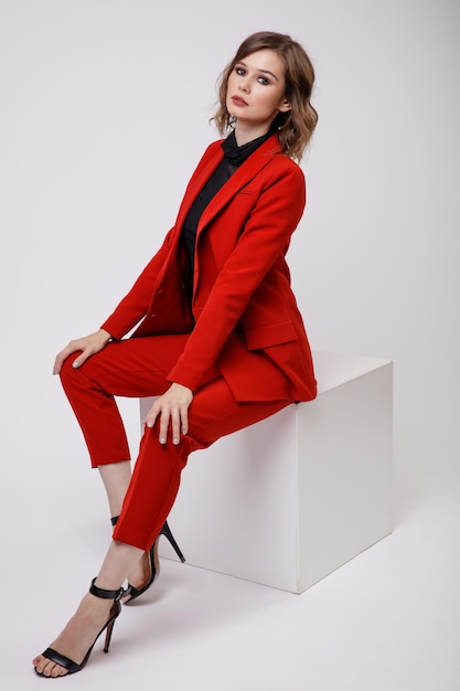 きれいな赤いスーツのジャケットのズボンの白い背景の上の黒いブラウスのエレガントな若い女性