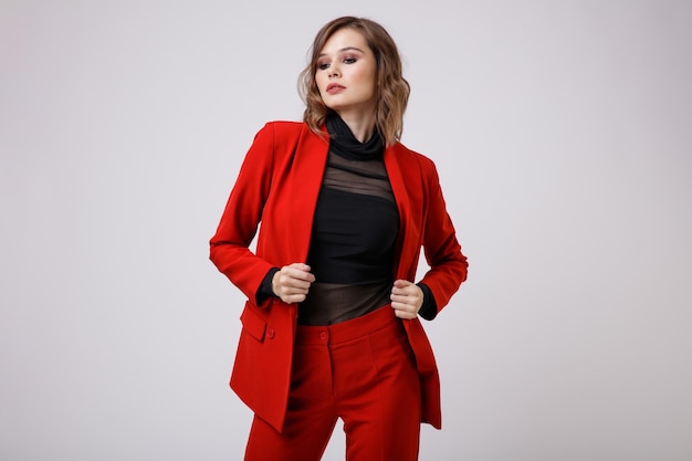 Elegant young woman in a pretty red suit jacket pants trousers black blouse on white background