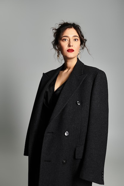 elegant young woman in sophisticated attire poses in studio against grey backdrop