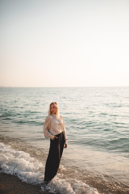 Elegant young woman wear stylish black pants and shirt standing in sea water over coast line outdoor