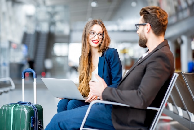 Elegant zakenpaar zit met laptop, telefoon en koffer in de wachtzaal op de luchthaven. Zakelijk reisconcept