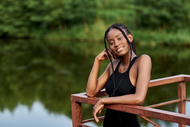 elegante afro-vrouw in mode-jurk staat in de buurt van een blauw meer op zonnige zomerdag