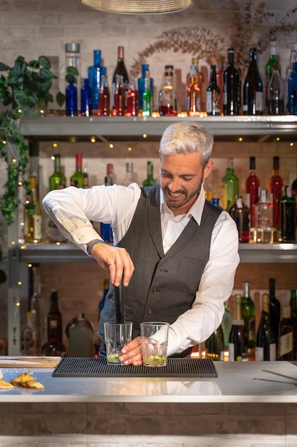 Elegante barman die cocktail Mojito maakt in nachtclub, ingrediënten toevoegt en deskundige drankjes maakt op toog