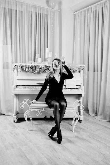 Elegante blonde girl wear on black dress against piano with christmas decoration