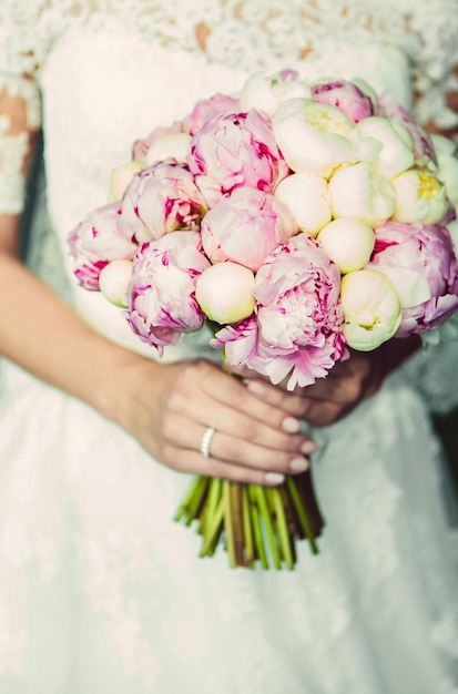 Elegante bruiloft boeket in de handen van de bruid. bruidsboeket van witte en roze pioenrozen. boeket met wit lint. Bruid hand met een trouwring.