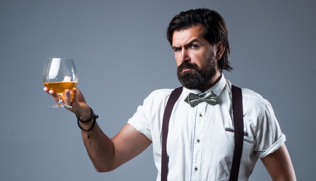 Elegante brutale man in formele kleding heeft verzorgd haar en drinkt whisky-alcohol