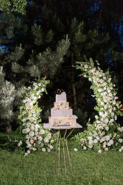 Elegante gelaagde bruidstaart verlicht met romantische lichten tegen een bloemrijke achtergrond in de buitenlucht