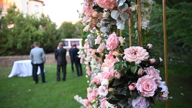 Elegante huwelijksboog met verse bloemen, vazen op de achtergrond van mensen. Boog, versierd met roze en witte bloemen die in het bos staan.