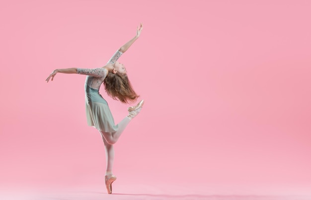 Elegante jonge ballerina in pointe-schoenen dansen op een delicate roze achtergrond
