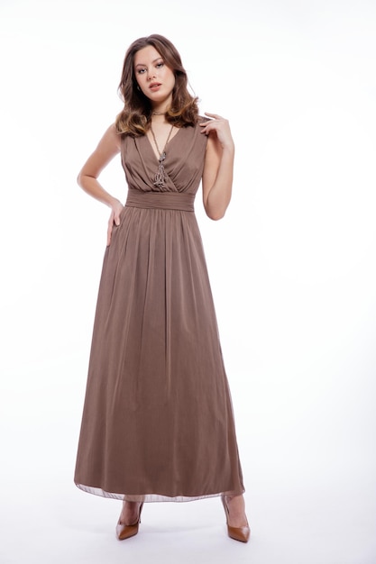 Elegante jonge vrouw in beige bruine jurk met een halsketting die zich voordeed op een witte achtergrond