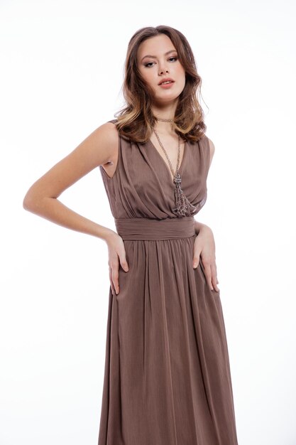 Elegante jonge vrouw in beige bruine jurk met een halsketting die zich voordeed op een witte achtergrond