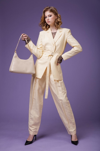 Elegante jonge vrouw in beige crème linnen colbert broek blazer handbad op paarse achtergrond