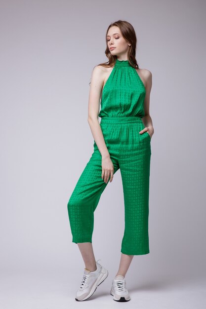 Elegante jonge vrouw in groene jumpsuit sneakers op witte achtergrond Studio Shot Full length