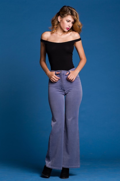 elegante jonge vrouw in jeans denim, zwarte top poseren op blauwe achtergrond