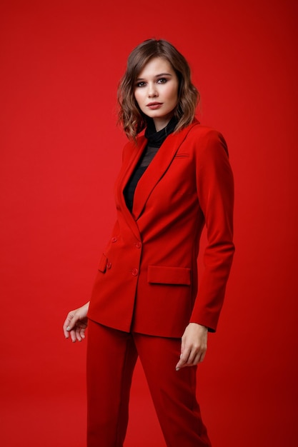 Elegante jonge vrouw in rood pak jasje broek broek zwarte blouse op achtergrond Monochroom