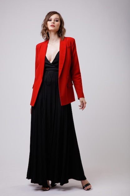 Elegante jonge vrouw in zwarte avondfeestjurk met diep decolleté rood jasje op witte achtergrond