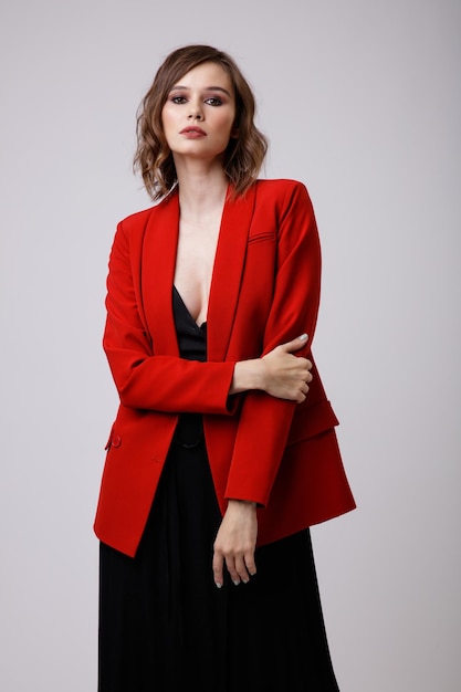 Elegante jonge vrouw in zwarte avondfeestjurk met diep decolleté rood jasje op witte achtergrond