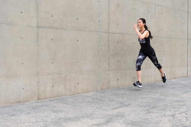 elegante jonge vrouwelijke jogger joggen op grijze achtergrond stoep in stadspark gebied training persoonlijke gezond en fitness door middel van marathon weglopen.