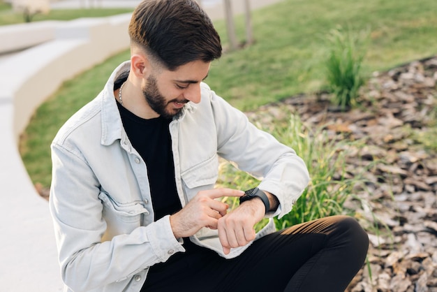 Elegante man met een baard die een smartwatch aanraakt, mannelijk gebruik van een draagbaar slim horloge buitenshuis