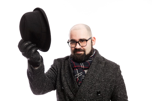 Elegante man met een baard in een jas. Hij nam zijn hoed af. Geïsoleerd op een witte muur.