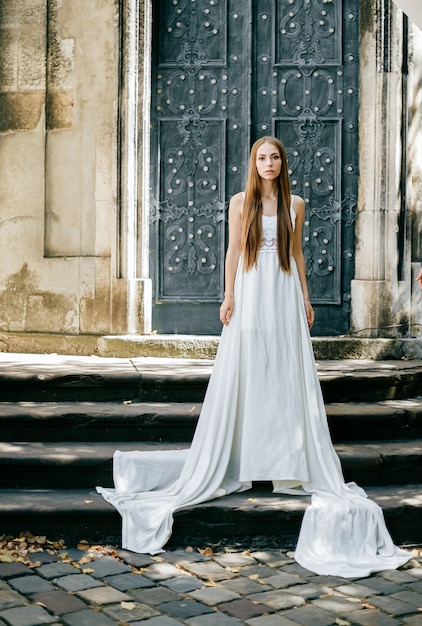 Elegante meisje in lange witte jurk poseren over oude deur