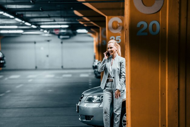 Elegante onderneemster die op mobiele telefoon in ondergronds autoparkeren spreekt.