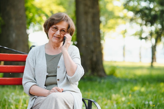 Elegante oudere vrouw in het shirt zit op een warme dag op de bank in een park